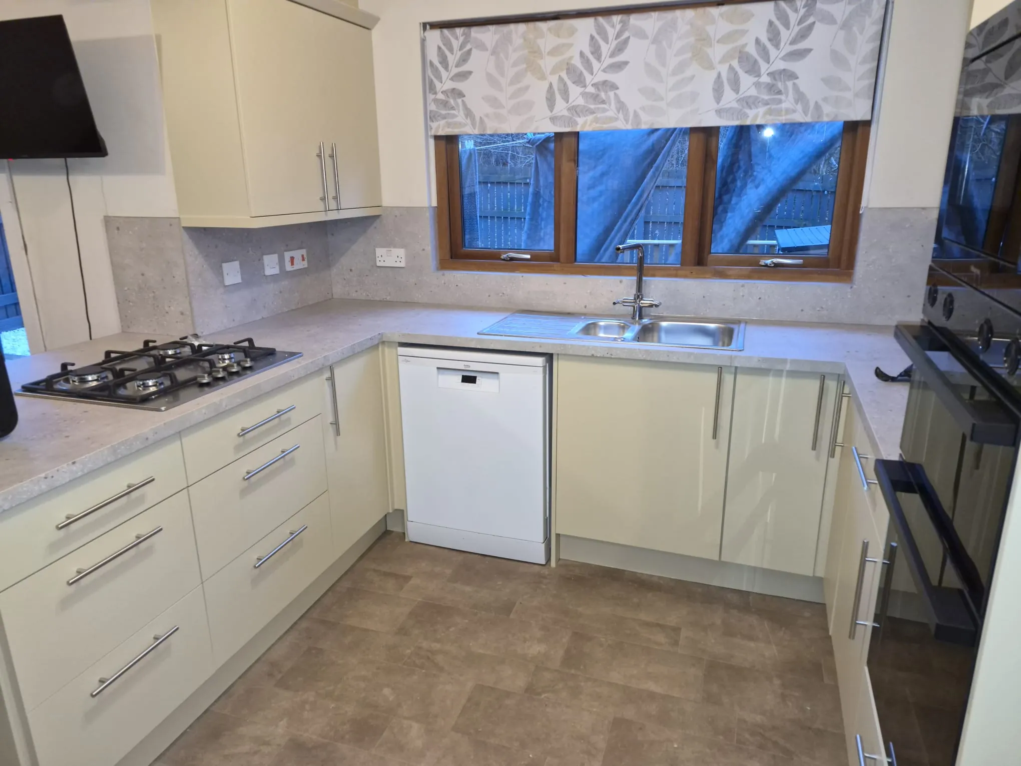 Cream gloss U-shaped fitted kitchen with grey speckled worktops, gas hob and stainless sink