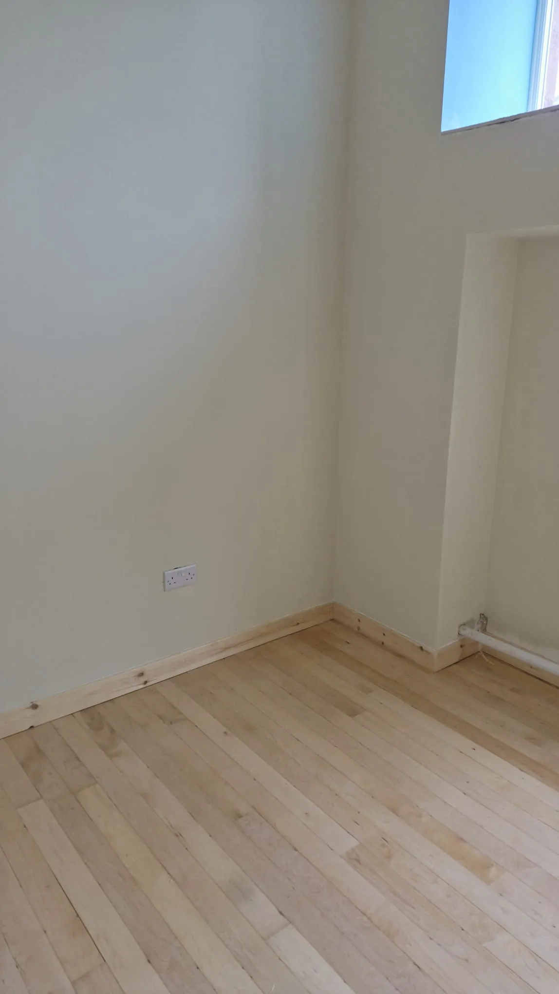 Finished room corner with painted walls, pine skirting and light hardwood strip floor