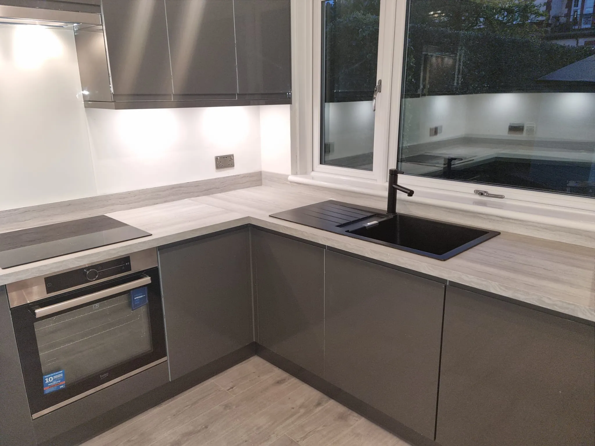 Grey gloss handleless kitchen with black composite sink, hob and stone effect worktop