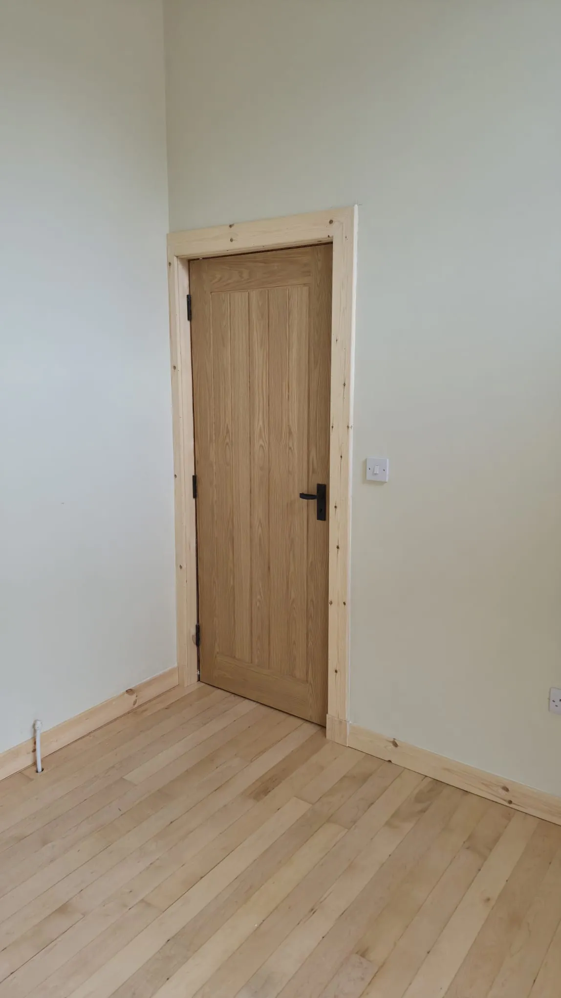 Oak cottage-style door with black handle, pine architrave and light hardwood floor