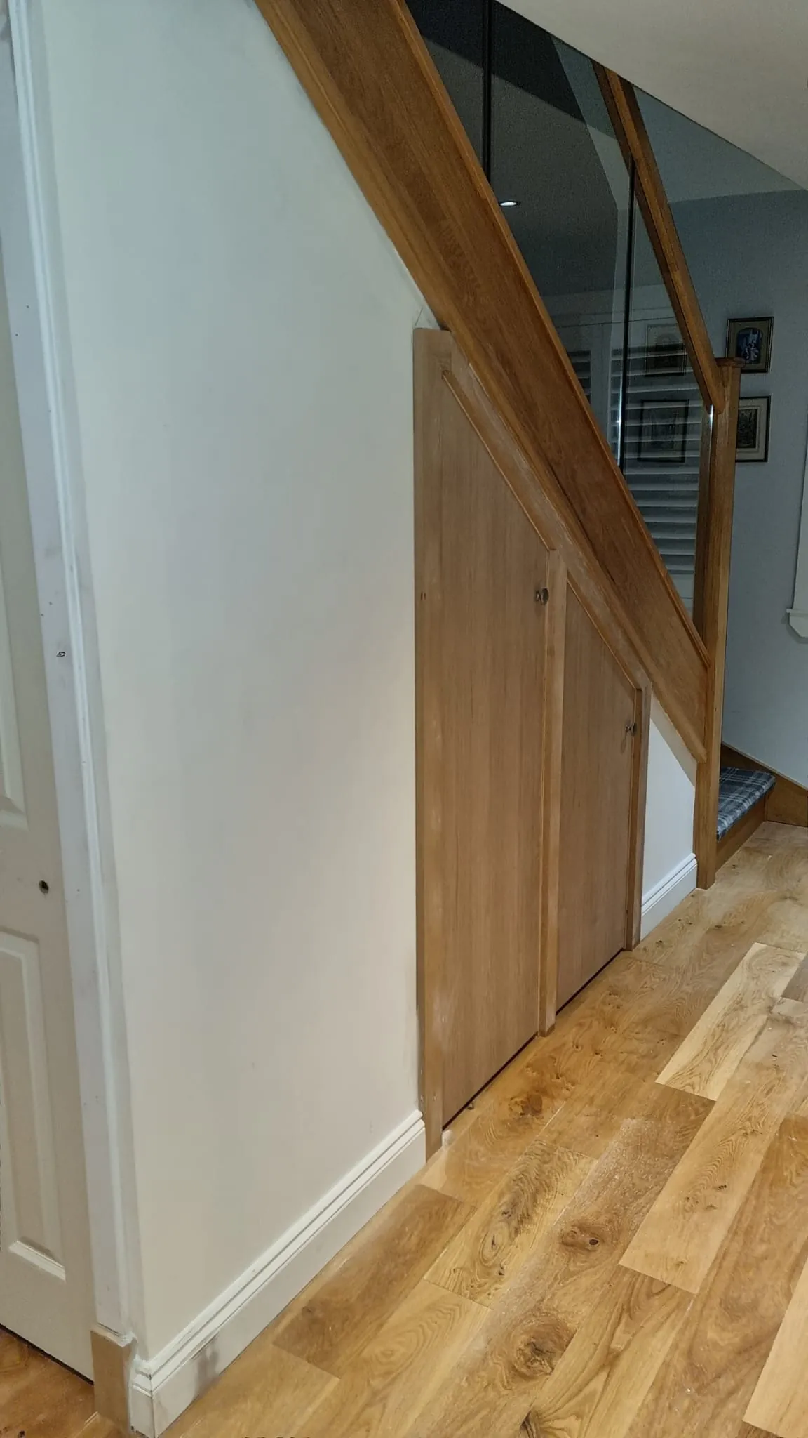 Oak under-stair cupboard doors beneath an oak and glass staircase on oak flooring
