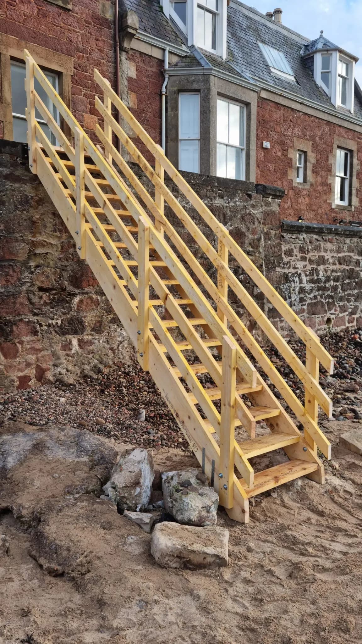 Timber stair with double handrails leading from a beach up a stone sea wall