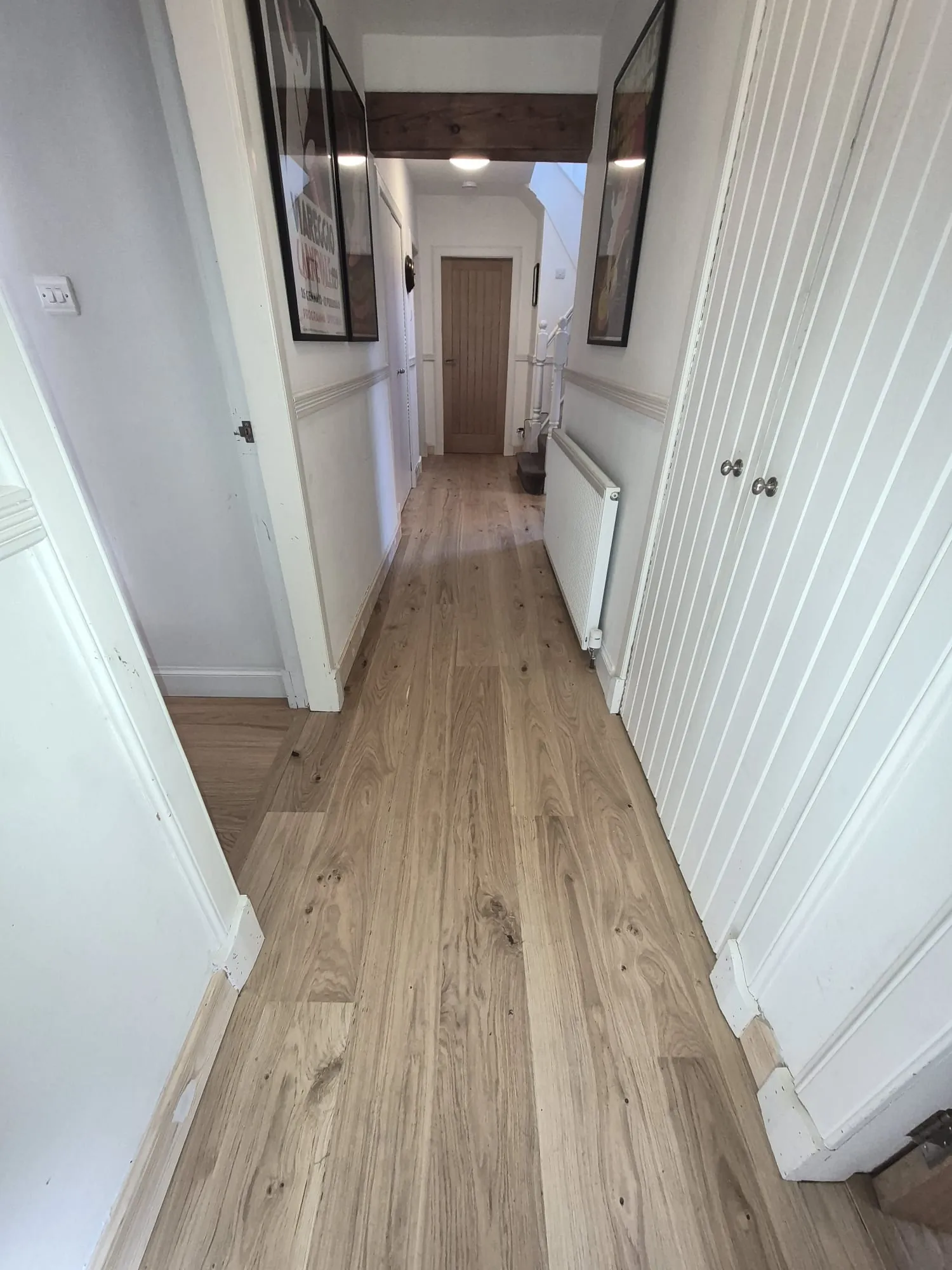 Wide plank oak flooring laid along a bright hallway with white panelled cupboard doors