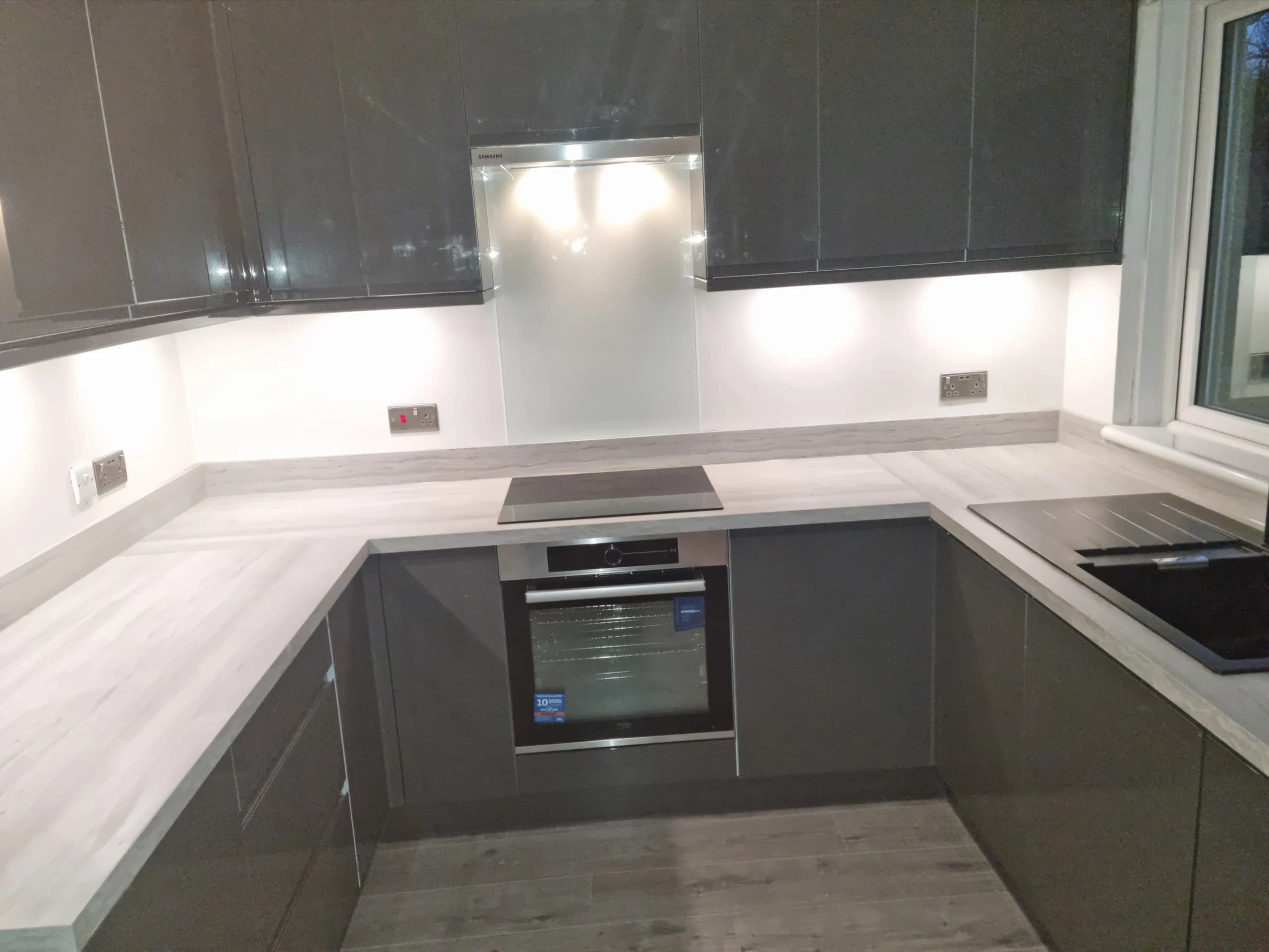 Grey handleless kitchen with under-cabinet lighting and stone-effect worktops
