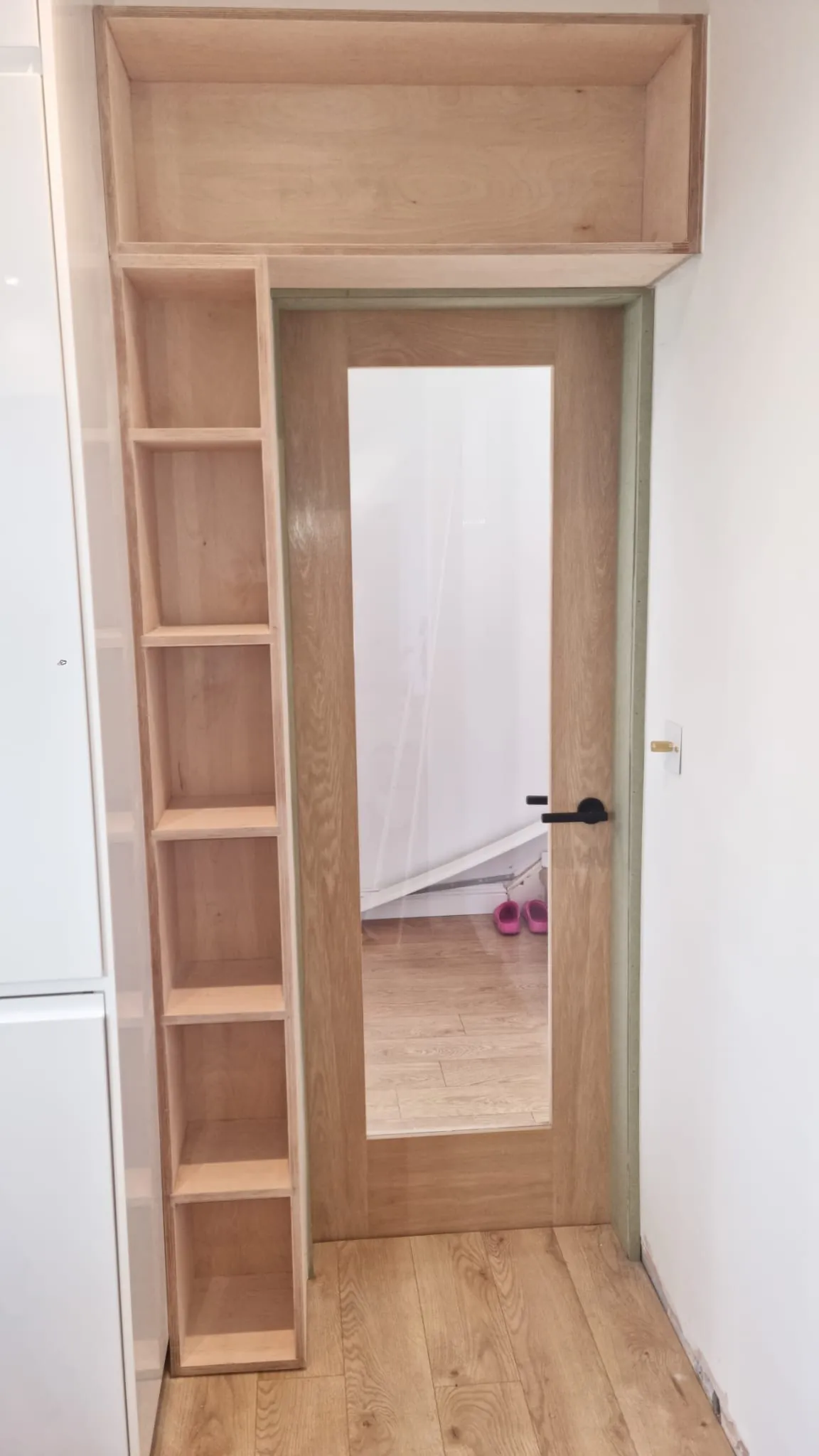 Bespoke plywood shelving and overhead storage built around an oak glazed internal door