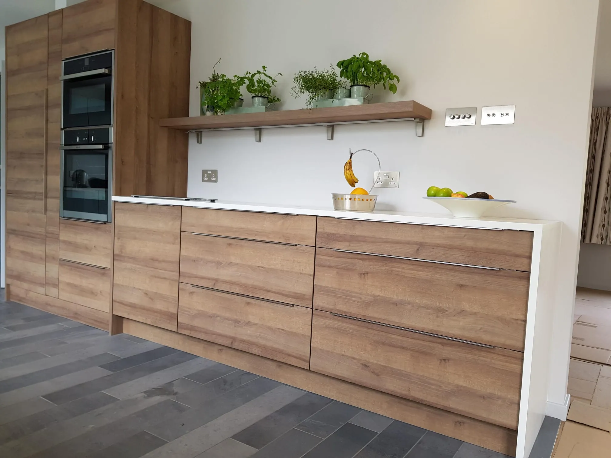 Oak effect handleless kitchen with white waterfall worktop, oven tower and floating shelf